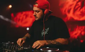 DJ in red cap and headphones mixes music on a console in a club with red lighting.