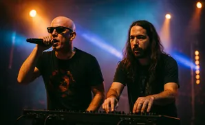 Two men performing on stage, one singing into a microphone, the other playing a keyboard, with stage lighting.