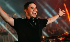 DJ with arms raised in excitement, wearing headphones around his neck.