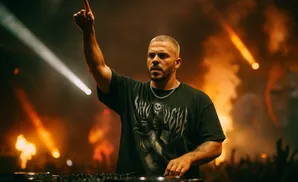 DJ with arm raised, silhouetted against stage lights and smoke.