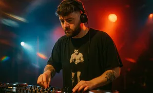 A DJ wearing headphones and a t-shirt with a boxer graphic, operating a soundboard in a dimly lit club.
