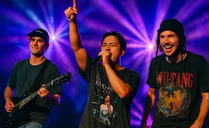 Three men performing on stage with purple and blue lights.