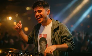 A happy DJ plays music at a club, illuminated by stage lights.