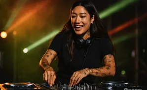 A smiling woman with tattoos on her arms is mixing music on a DJ setup.