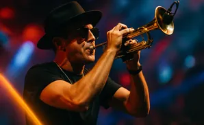 A man in a black hat and sunglasses plays a trumpet on a dimly lit stage with colorful lights.