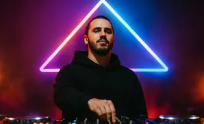 DJ performing in front of a neon triangle with purple and blue lighting.