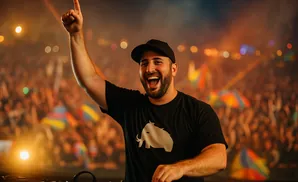 DJ with hand raised in excitement, smiling at a crowded music festival.