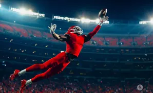 A football player in a red uniform leaps to catch a pass in a stadium under bright lights.