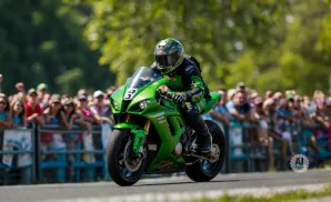 A green motorcycle rider speeds past a blurred crowd at a race.