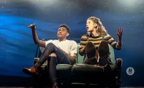 A young Black man and woman sit on a couch, looking up at a starry night sky.