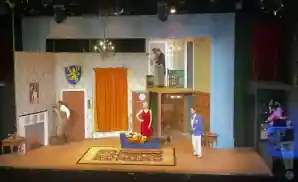 six characters of the play that goes wrong, sharing a scene on stage. the stage lighting controller is right next to the stage.