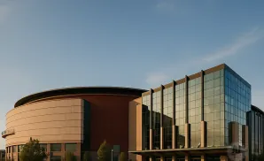 Modern building with a curved tan section and a glass-fronted section under a clear blue sky.