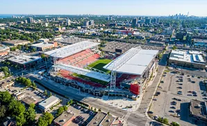 Aerial view of a red-seated stadium surrounded by urban development, with a city skyline in the distance.