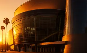 Modern glass building bathed in golden sunset light with palm trees.