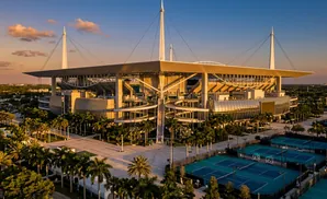 Sunset over a large stadium with tennis courts and palm trees.