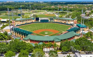 Aerial view of a baseball stadium with multiple fields and surrounding trees and buildings.