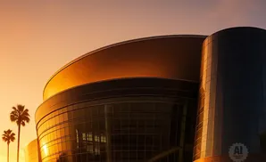 Modern glass building with curved roof and palm trees at sunset.