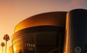 Sunset casts a golden glow on a modern building with glass facades, framed by palm trees.