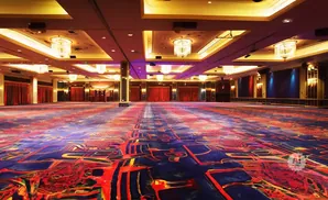 A grand ballroom with a vibrant, abstract carpet in shades of blue, red, and yellow, illuminated by ornate chandeliers.