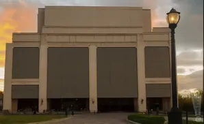 A large, light-colored building with large gray panels and a street lamp in front during sunset.