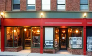 A red-trimmed shop with large windows displaying merchandise, lit by warm interior lights.