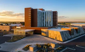 Aerial view of a modern hospital with a tall, brown tower and a multi-faceted, angular wing.