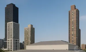 A multi-story building with a grey roof in the foreground, and three skyscrapers of varying heights in the background against a clear blue sky.