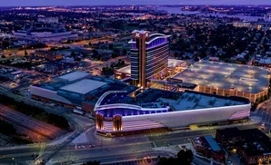 Aerial view of the colorful MotorCity Casino Hotel at night, with city lights and a bridge in the background.