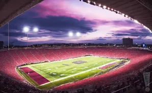 A full football stadium with red seats, a green field, and a purple sunset sky.