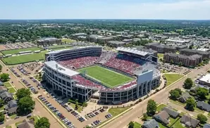 Aerial view of a packed football stadium surrounded by university buildings and parking lots.
