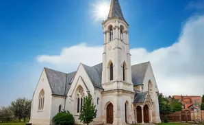 A white church with a tall steeple under a sunny blue sky with clouds.
