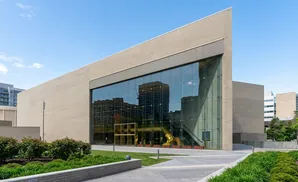 Modern brick building with a large glass facade reflecting the surrounding cityscape and sky.