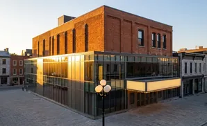 A modern glass-fronted building with a brick upper section, next to older stone buildings.