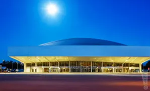 Modern, brightly lit convention center with a curved roof under a clear blue sky at dusk.
