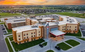 Aerial view of a modern hotel with a parking garage and surrounding suburban landscape at sunset.