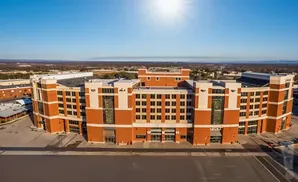 Aerial view of a large brick building with white accents, a bright sky overhead, and a distant landscape.