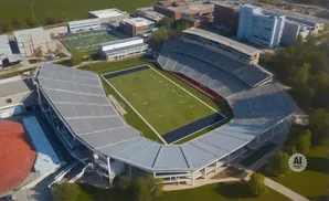 Aerial view of a football stadium with green field and bleachers, surrounded by buildings and trees.
