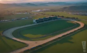 Aerial view of a greyhound racing track with grandstands and rolling hills in the background.