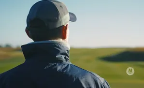 Man in a baseball cap and jacket looks out over a green, rolling landscape.