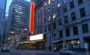 A vintage theater marque glows with lights on a city street at dusk.