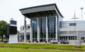 Modern building with glass facade, large screens, and flags outside.