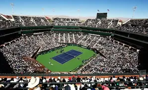 An aerial view of a packed tennis stadium during a match, with spectators filling the grandstands.