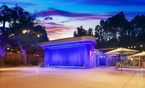 Outdoor stage at dusk with blue lights, string lights, and yellow umbrellas.