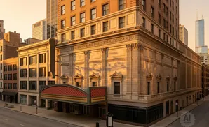 Golden hour light on an ornate theater facade with surrounding brick buildings and a distant skyscraper.