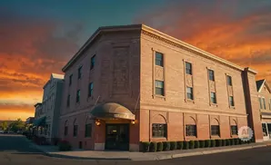 Brick building with ornate details and arched windows under a dramatic orange and blue sunset sky.