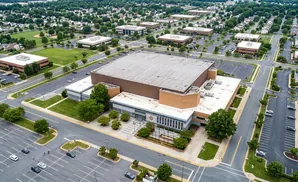 Aerial view of a large building complex with parking lots and surrounding greenery.
