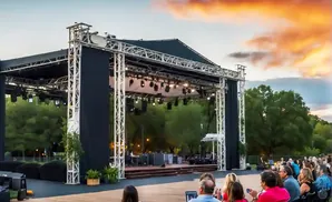 An outdoor concert stage at sunset with an audience seated in front.
