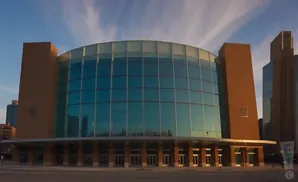A modern glass and brick building with a curved facade under a cloudy sky.