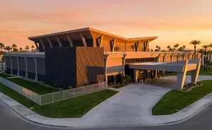 Modern building with sharp angles and a covered entrance, surrounded by palm trees at sunset.