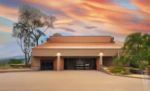 Modern building with a copper roof at sunset, surrounded by trees and desert landscape.